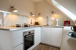 A modern kitchen with white cabinetry, a Bosch oven, a coffee maker, and a red kettle.