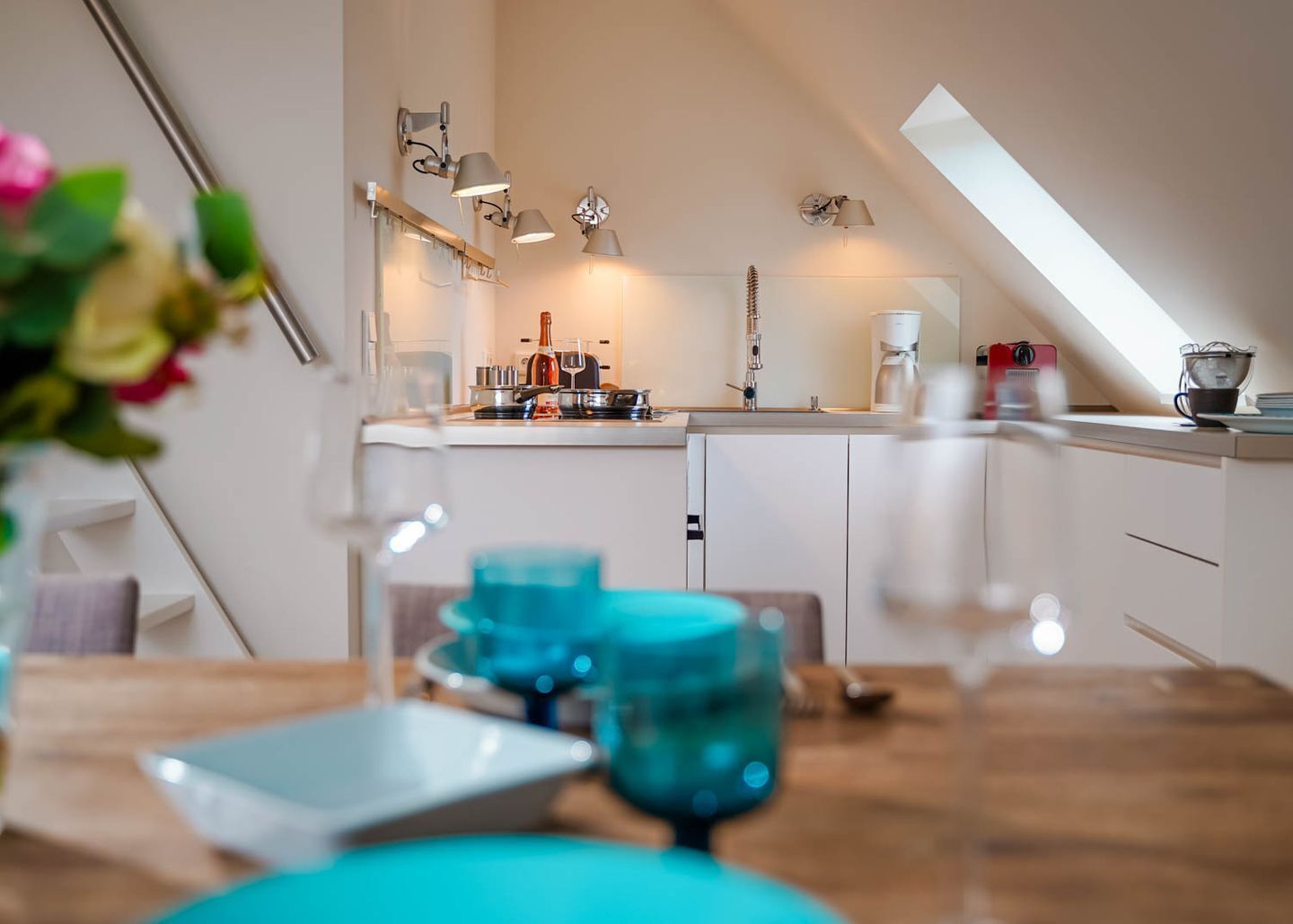 Ett modernt kök med vita skåp, en bänkskiva och en hängande lampa. På bänkskivan står en kaffebryggare och en vattenkokare.
