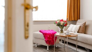 Una sala moderna con un sofá, una mesita con un florero y una manta rosa sobre un reposapiés.