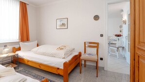 Un dormitorio con una cama de madera, una mesita de noche con lámpara, una silla y un cuadro en la pared.