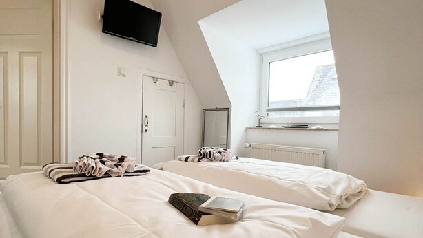 A bedroom with a bed, a flat-screen TV, a window, and a door. - East - Relaxed island life: Cozy vacation apartment in Westerland on Sylt (Sylt)