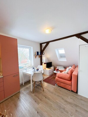Une pièce compacte et bien éclairée, comprenant un coin repas, une kitchenette et un espace salon confortable avec un canapé et une petite table.