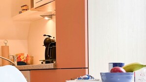 A modern kitchen with a white chair, a table with a blue bowl, and a fruit bowl. - East - Relaxed island life: Cozy vacation apartment in Westerland on Sylt (Sylt)