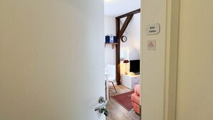 A room with a wooden floor, a white door, a small desk with a lamp, a chair, and a pink sofa. - East - Relaxed island life: Cozy vacation apartment in Westerland on Sylt (Sylt)