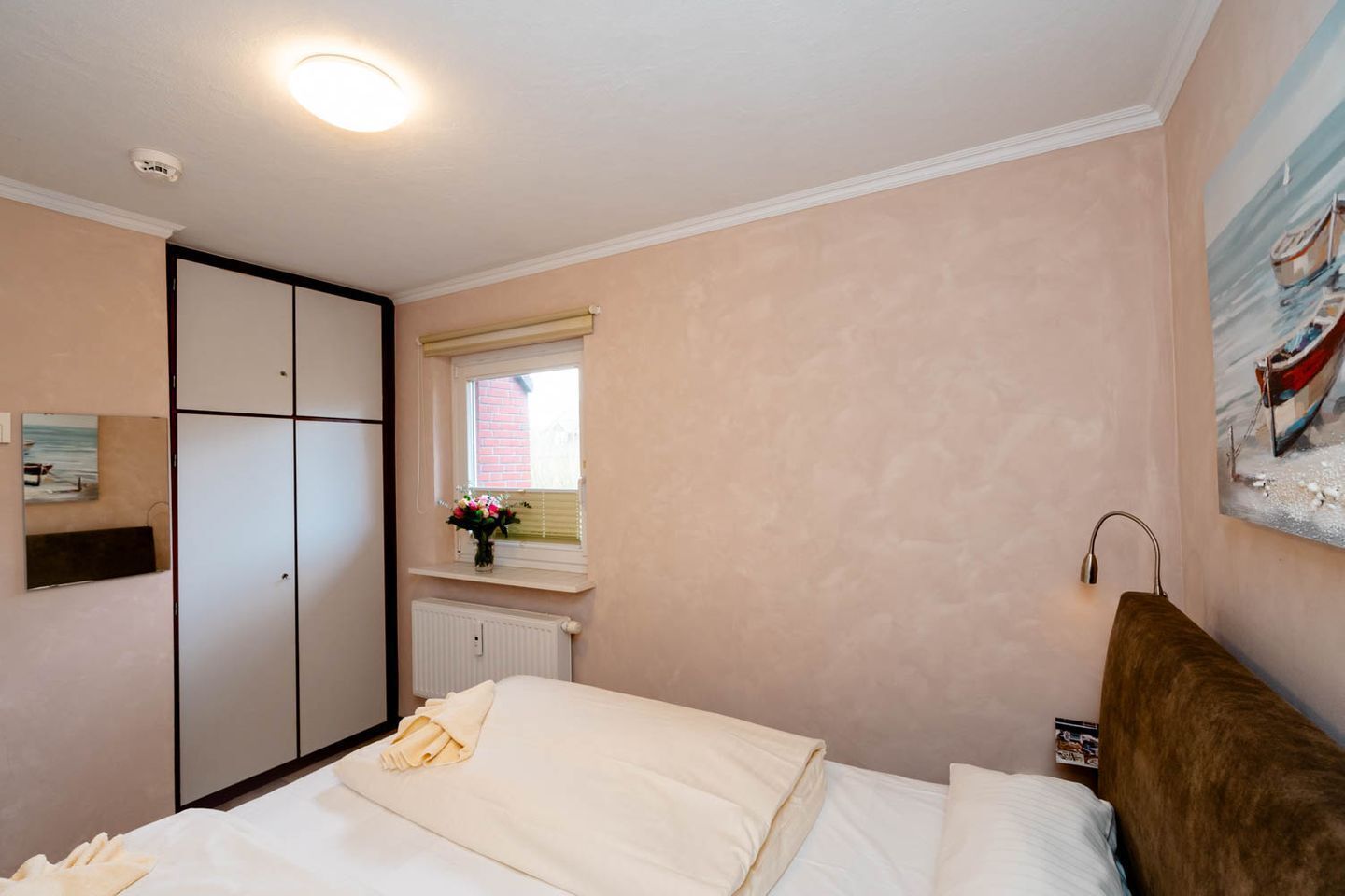 Ein Schlafzimmer mit Bett, Kleiderschrank, Fenster mit Meerblick und einem Gemälde an der Wand.