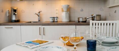 Een eettafel gedekt met borden, glazen en een tijdschrift in een moderne keuken met witte kasten en een magnetron.