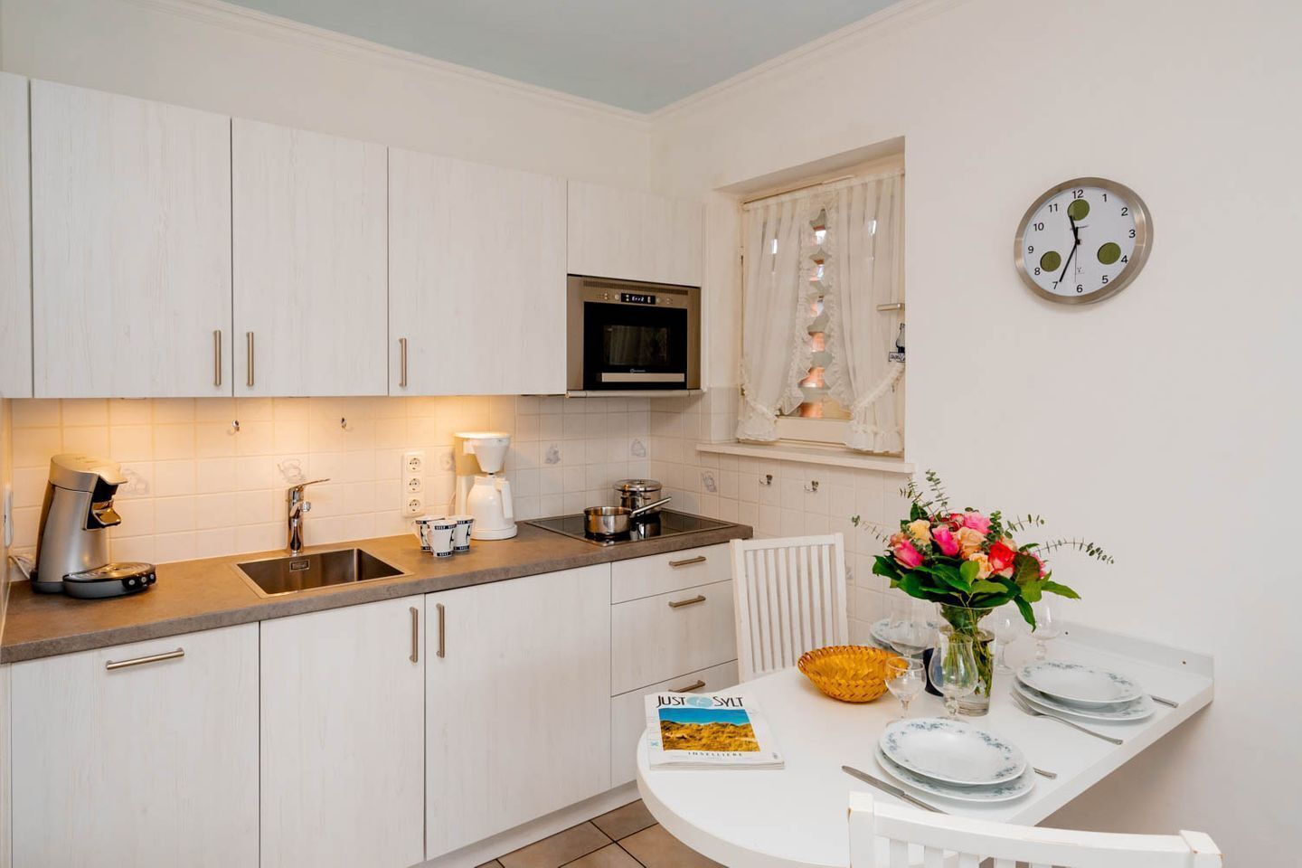A modern kitchen with white cabinets, a built-in microwave, and a dining area with a white table set for two.