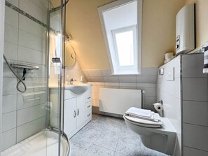 Une salle de bain moderne dotée d’une douche à parois de verre, d’un lavabo avec un meuble-vasque, de toilettes et d’une fenêtre laissant entrer la lumière naturelle.