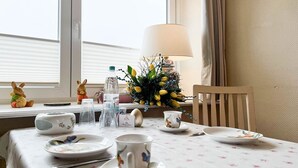 Una mesa de comedor dispuesta con platos, tazas, cubiertos, una lámpara, una botella de agua y elementos decorativos como una figurita de conejo y un jarrón con flores.