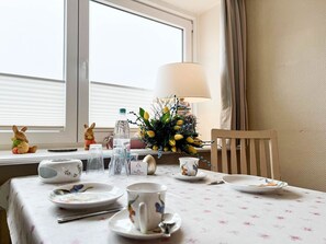 Une table à manger dressée avec des assiettes, des tasses et des couverts, une lampe, une bouteille d’eau et des objets décoratifs, comme une figurine de lapin et un vase de fleurs.
