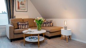 Un salon chaleureux avec un canapé, une table basse ronde, une table d’appoint avec une lampe et un tableau accroché au mur.
