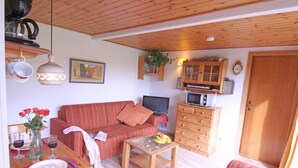 Una sala de estar acogedora con sofá, mesa de centro, televisor, armarios de madera y un comedor con mesa dispuesta para dos.