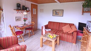 Una sala de estar acogedora con un sofá, sillas, una mesa de centro con fruta, un televisor y un techo de madera.