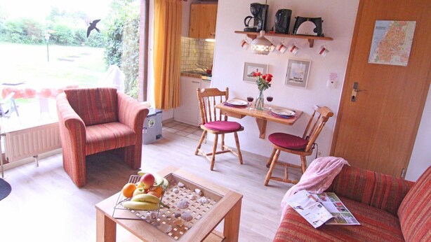 Una sala acogedora con sofá, sillón, mesa de comedor y una mesa baja con frutas y conchas marinas.