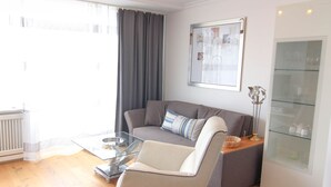Una sala de estar moderna con un sofá gris, una mesa de centro de vidrio y un aparador de vidrio con objetos decorativos.