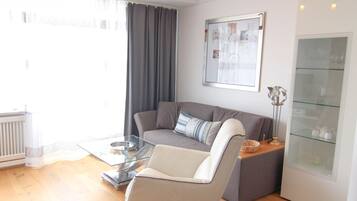 A modern living room with a grey sofa, a glass coffee table, and a glass cabinet with decorative items.