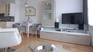 Una sala moderna con un sofá, una mesa de centro de vidrio, un televisor y una cocina con armarios y una mesa de comedor.