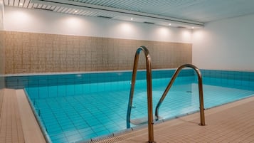 An indoor swimming pool with clear blue tiles, a tiled floor, and a metal pool ladder.