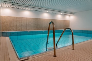 Una piscina interior con baldosas azules brillantes, suelo de cerámica y una escalera metálica.
