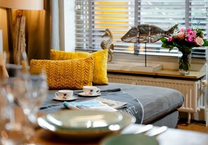 Ein gemütliches Zimmer mit einem Bett, einem Fenster mit Jalousien, einer Blumenvase und einem dekorativen Vogel auf der Fensterbank.