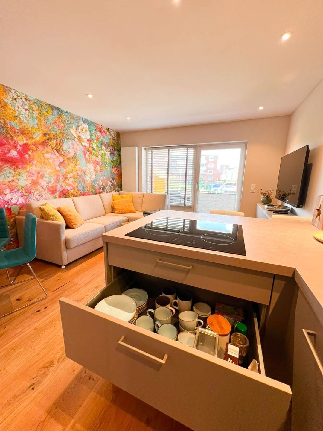A modern kitchen with a built-in stove, a dining area with a sofa, and a colorful floral wall.
