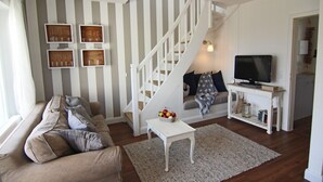 Un salon comprenant un canapé, une table basse, un téléviseur, un escalier et des étagères fixées au mur.