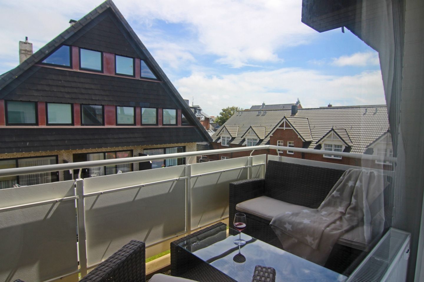 Ein Balkon mit Tisch und Stühlen, einer gepolsterten Bank und Blick auf Wohnhäuser.
