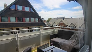 Un balcon avec une table et des chaises, un banc rembourré et une vue sur des immeubles d’habitation.