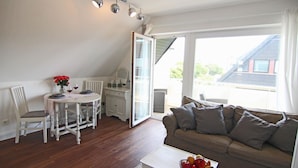 Un salon chaleureux comprenant un coin repas, un canapé et une table sur laquelle se trouve un panier de fruits.
