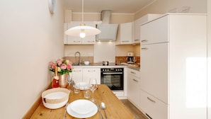 A compact kitchen with white cabinets, a wooden dining table set with plates, glasses, and cutlery, and a vase with flowers. - Alea - A modern and bright vacation apartment in the heart of Westerland. (Sylt)