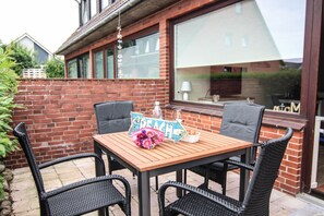 An outdoor patio with a wooden table, four wicker chairs, a decorative sign, and a glass bottle. - Alea - A modern and bright vacation apartment in the heart of Westerland. (Sylt)