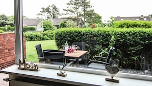 A window with a view of a backyard patio area, including a table with chairs and a grill. - Alea - A modern and bright vacation apartment in the heart of Westerland. (Sylt)