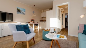 A modern living room with a sofa, a coffee table, and a television. - Alea - A modern and bright vacation apartment in the heart of Westerland. (Sylt)
