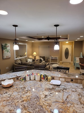 A kitchen with a granite countertop, a dining area with a table and chairs, and a living room with a sofa and a coffee table.