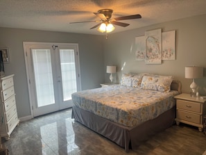 A bedroom with a bed, two bedside tables, a ceiling fan, and a door with blinds.