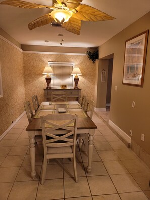 A dining room with a wooden table, chairs, a ceiling fan, and two lamps.