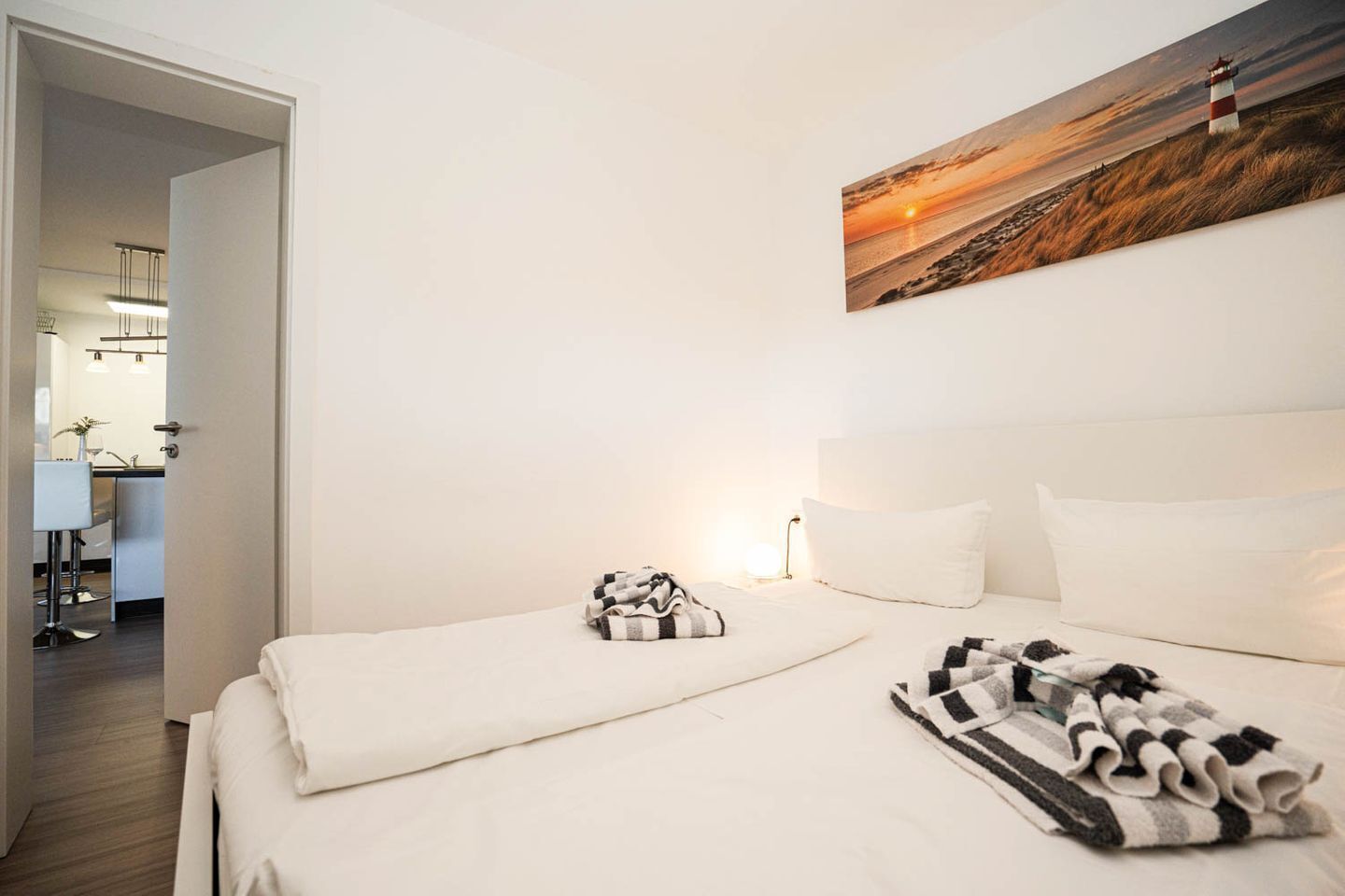 Et hotelværelse med en seng, et maleri af en solnedgang og udsigt til et køkken og spiseområde.