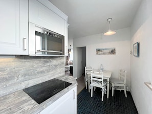 Une cuisine compacte avec des meubles blancs, une plaque de cuisson à induction noire, un four à micro-ondes et un coin repas comprenant une table et des chaises.