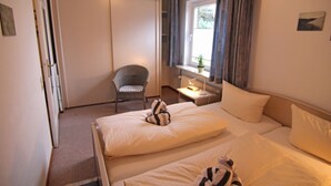 Camera d'albergo con due letti, una sedia, una finestra con tende e un tavolino con lampada.