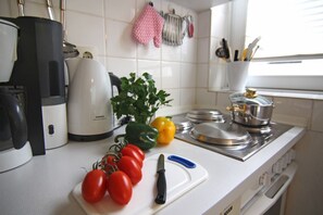 Keittiössä on valkoiset laatat, Siemensin kahvinkeitin, leikkuulauta, jossa on tomaatteja ja veitsi, sekä liesi.