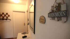 Un corridoio con una porta bianca, uno specchio, una targa di legno con la scritta 'MOIN MOIN' e una piccola targa con del testo.