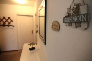 A hallway with a white door, a mirror, a wooden sign with 'MOIN MOIN' and a small plaque with text.