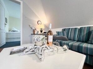 Una sala de estar con un sofá a rayas, una mesa de centro con una botella de vino, una lámpara y una pequeña mesita auxiliar con adornos.