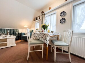 A cozy living room with a dining area, a sofa, and a table set for two. - Tessa in Haus Käpt'n Andresen - A vacation apartment ideal for relaxing and (Sylt)