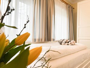 Un dormitorio con una cama, una ventana con cortinas y una planta con flores amarillas.