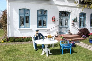 Un bâtiment blanc avec des volets bleus et un petit jardin agrémenté d’une statue blanche, d’une table et de chaises.
