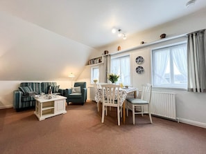 A cozy living room with a sofa, a dining table with chairs, a lamp, and a radiator. - Tessa in Haus Käpt'n Andresen - A vacation apartment ideal for relaxing and (Sylt)