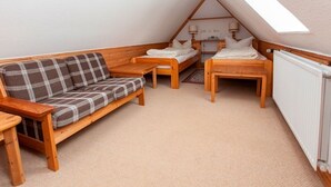Une chambre mansardée chaleureuse, avec un canapé en bois, deux lits simples, une petite table et un radiateur.