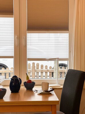 A dining area with a table set for two, a black kettle, a bowl of fruit, and a cup.