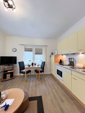 A compact kitchen with a dining area, a TV, and a clock on the wall.